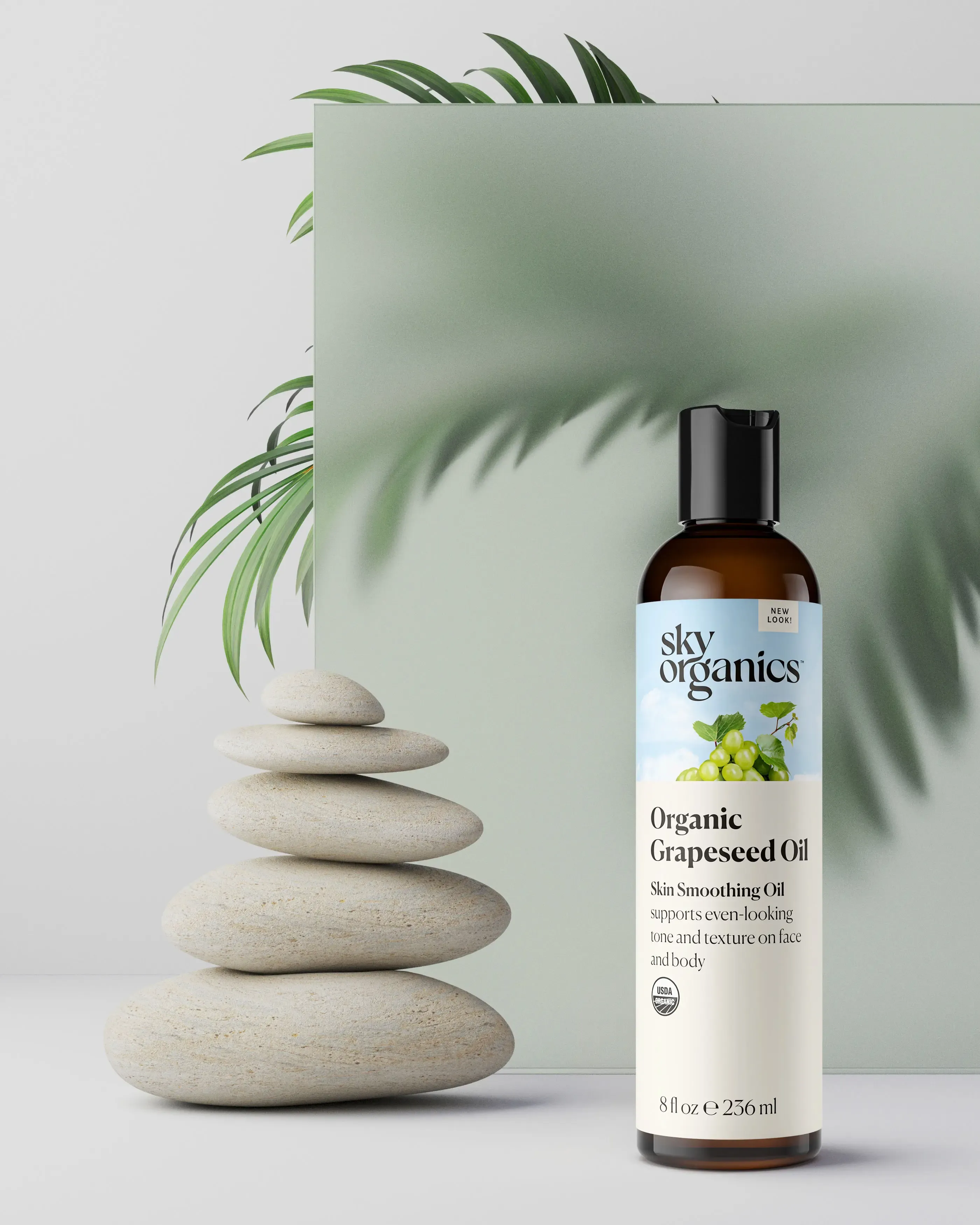 3D render of a Sky Organics Organic Grapeseed Oil bottle beside stacked stones and a palm leaf